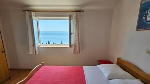 Um quarto com cama, janela com cortinas e vista para o mar.
