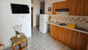 A compact kitchen with wooden cabinets, a white refrigerator, a small countertop with a sink, and a television mounted on the wall. - Apartments Rubić - TwoBedroom Apartment with Loggia and SeaView (4) (Omis)