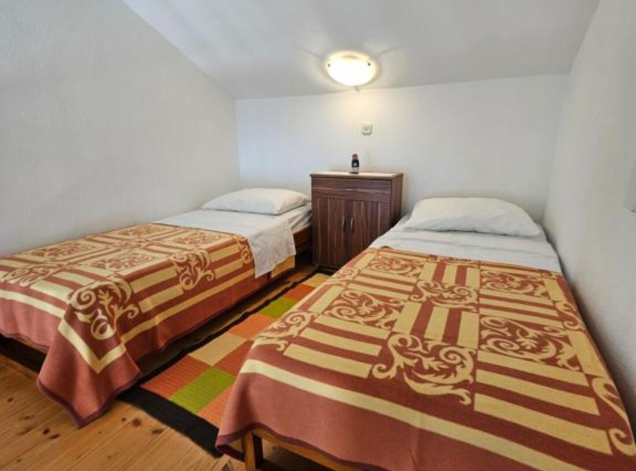 A small, clean room with two single beds, a wooden nightstand, and a ceiling light.
