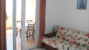 A living room with a sofa, a dining table with chairs, and a sliding glass door leading to an outdoor area. - Apartments Rubić - TwoBedroom Apartment with Loggia and SeaView (5) (Omis)