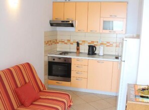 A compact kitchen with a stove, oven, and a small countertop. There is a sofa with striped cushions in the adjacent living area. - Apartments Rubić - Studio Apartment with Balcony and SeaView (6) (Omis)