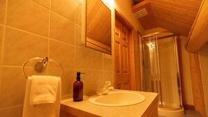 A bathroom with a wooden vanity, a sink, a mirror, a towel rack, and a shower enclosure. - Serene Lakeside Escape – Juniper Lodge, Lac La Hache (Lac la Hache)