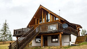 A wooden cabin with a balcony, a staircase, and a satellite dish. - Serene Lakeside Escape – Juniper Lodge, Lac La Hache (Lac la Hache)