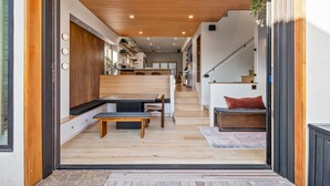 Um interior moderno com um banco de madeira, uma escada e vista para a cozinha.