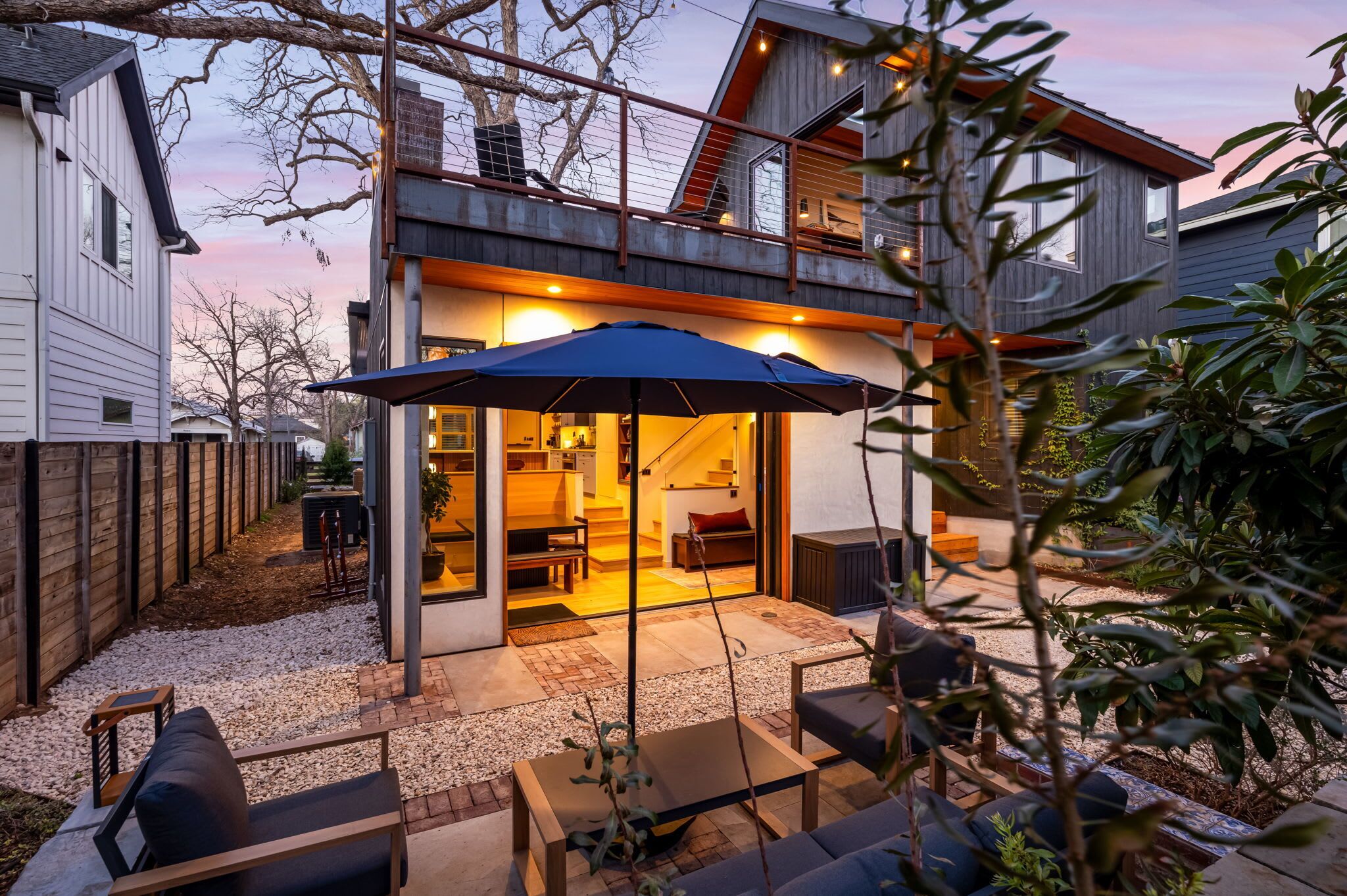 A modern house with a covered patio, outdoor seating, and a staircase leading to an upper level.