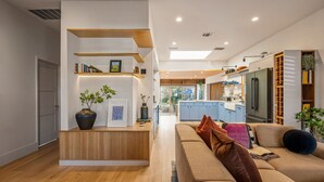 Uma sala de estar moderna com um balcão de atendimento de madeira, um sofá e uma cozinha ao fundo.
