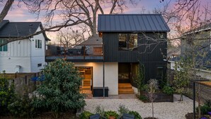 Uma casa moderna de dois andares com varanda, um pequeno jardim e área de estar externa.