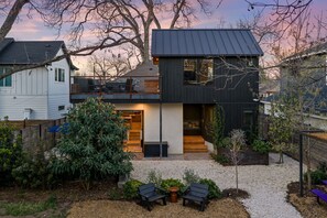 Ein modernes, zweistöckiges Haus mit Balkon, kleinem Garten und Sitzgelegenheit im Freien.
