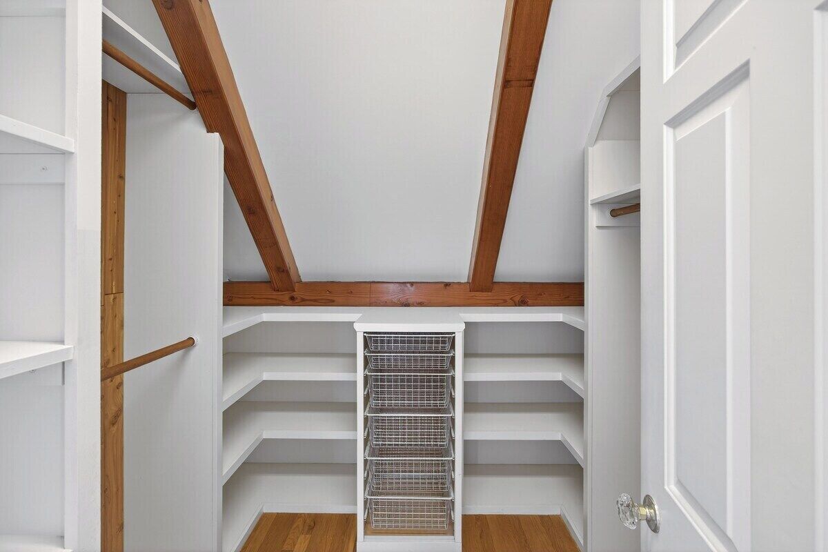 A narrow, white-walled room with wooden beams on the ceiling, a central vent, and a white door with a silver handle.