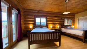 A log cabin bedroom with a large bed, a smaller bed, and a window overlooking a scenic view.