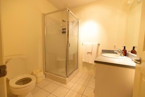 A bathroom with a toilet, a glass-enclosed shower, and a sink with a mirror. - Spacious Eagle’s Nest Cabin – Lakeside Escape at Our Gathering Place (Lac la Hache)