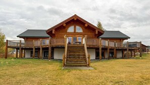 A large wooden house with a central staircase leading to a front door, surrounded by a grassy area.