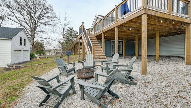 Eine Terrasse mit Adirondack-Stühlen und einem Feuerkorb, Holz-Geländer und eine Treppe zu einem überdachten Bereich.