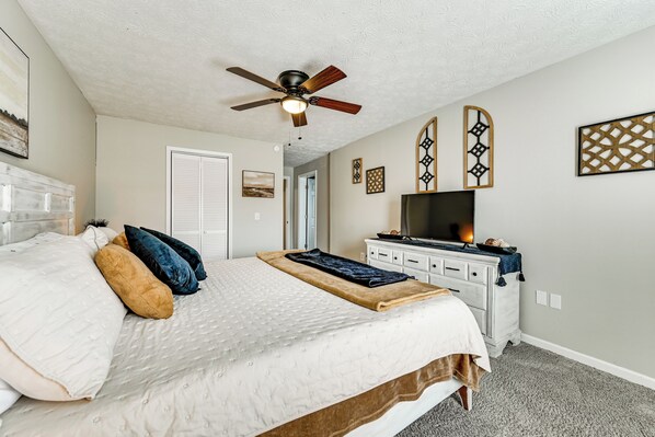 A bedroom with a bed, a ceiling fan, a dresser, a TV, and decorative wall art. - Lake Days & Fireside Nights! Updated Burnside Home (Burnside)