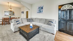 Ein Wohnzimmer mit einer Eckcouch, einem Couchtisch und einer dunklen Holzkiste. Im Hintergrund ist eine Essecke mit einem Holztisch und Stühlen sowie eine Küche zu sehen.