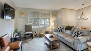 A modern living room with a sofa, armchair, coffee table, and a TV mounted on the wall. - 6 Mi to Dtwn Toledo! Family-Friendly Haven w/ Deck (Toledo)