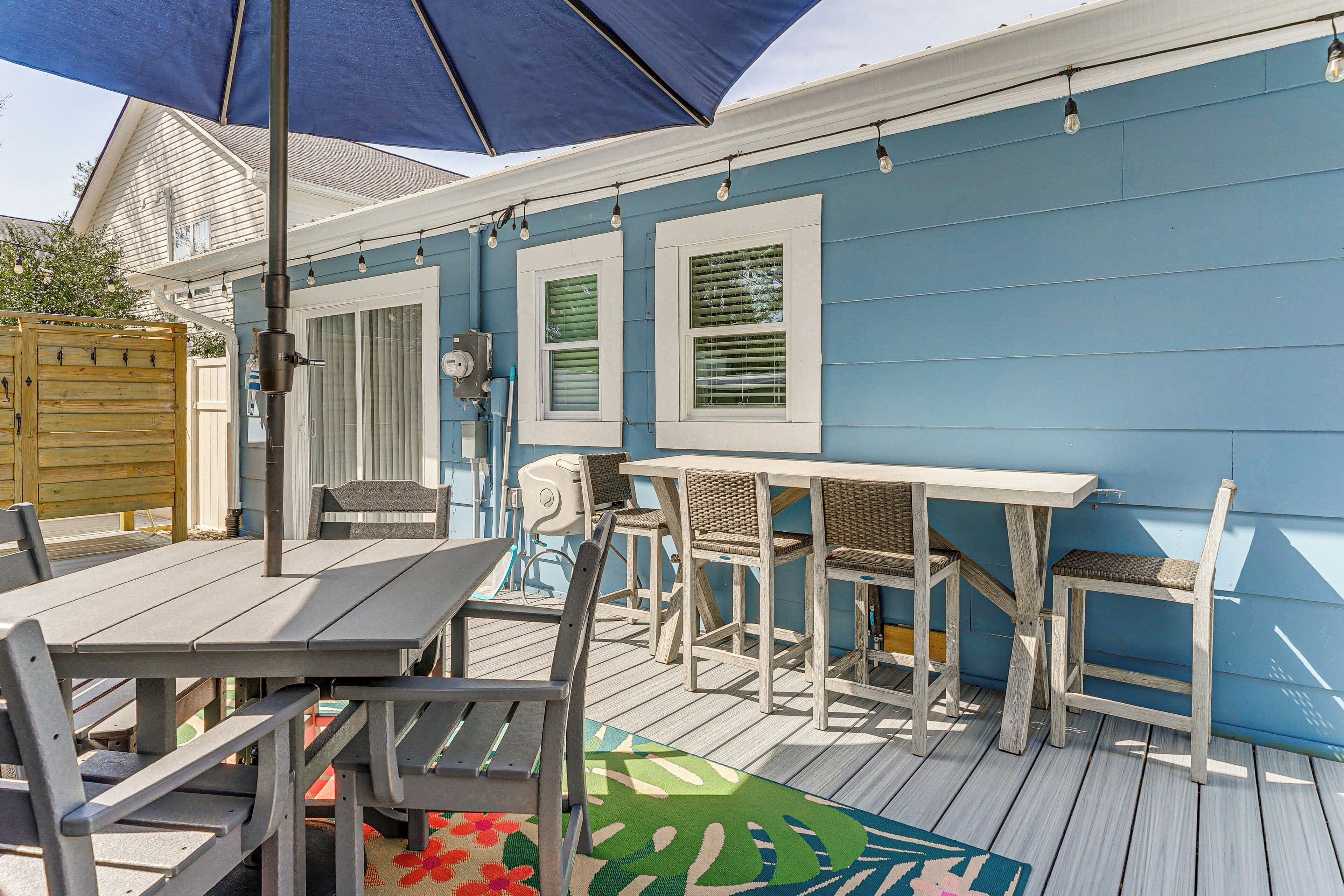 Eine Terrasse im Freien mit Tisch und Stühlen, ein Holzdeck und eine blaue Hauswand.