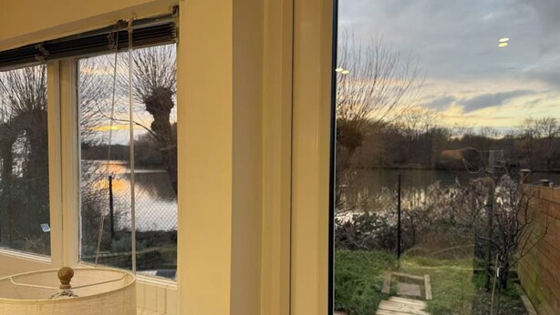 A room with large windows overlooking a garden and a body of water. - Lakeside Haven in London (London)
