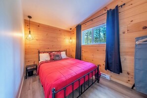 A wooden-paneled bedroom with a bed, a window with curtains, and a hanging light fixture.