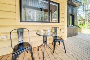 A wooden cabin with a deck, two chairs, a table, and a large window.