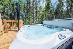 A hot tub on a wooden deck surrounded by trees.