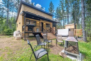 A cabin with a deck, outdoor seating, and a wood-burning stove.