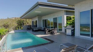 A modern house with a swimming pool, outdoor seating, and a grill area. - Ocean View Luxury + Sunset Terrace | Gated Resort (Del Coco Beach)