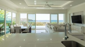 A modern kitchen with a large island, a dining area, and a sofa set. - Ocean View Luxury + Sunset Terrace | Gated Resort (Del Coco Beach)