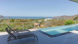 A rooftop pool with lounge chairs, overlooking a coastal landscape with hills and a clear sky. - Ocean View Luxury + Sunset Terrace | Gated Resort (Del Coco Beach)