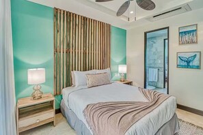A bedroom with a bed, two bedside tables, a wall-mounted lamp, a wooden slat partition, and artwork on the wall. - Modern Condo + Pool Access | Gated Community (Coco)