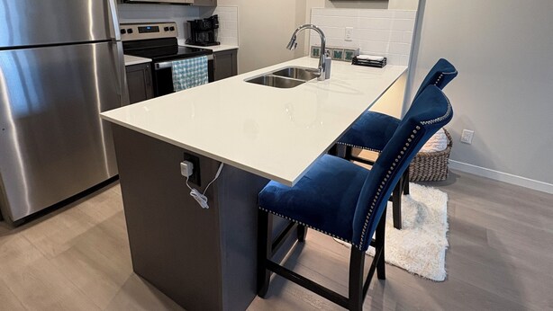 Een moderne keuken met een centraal eiland, roestvrijstalen apparatuur en een blauwe gestoffeerde stoel.