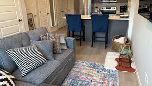 Een moderne keuken met roestvrijstalen apparatuur, een grijze bank met gestreepte kussens en een kleurrijk vloerkleed.