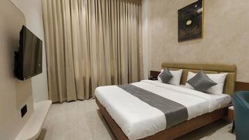 Quarto de hotel com uma cama grande, televisão de tela plana na parede e janela com cortinas bege.
