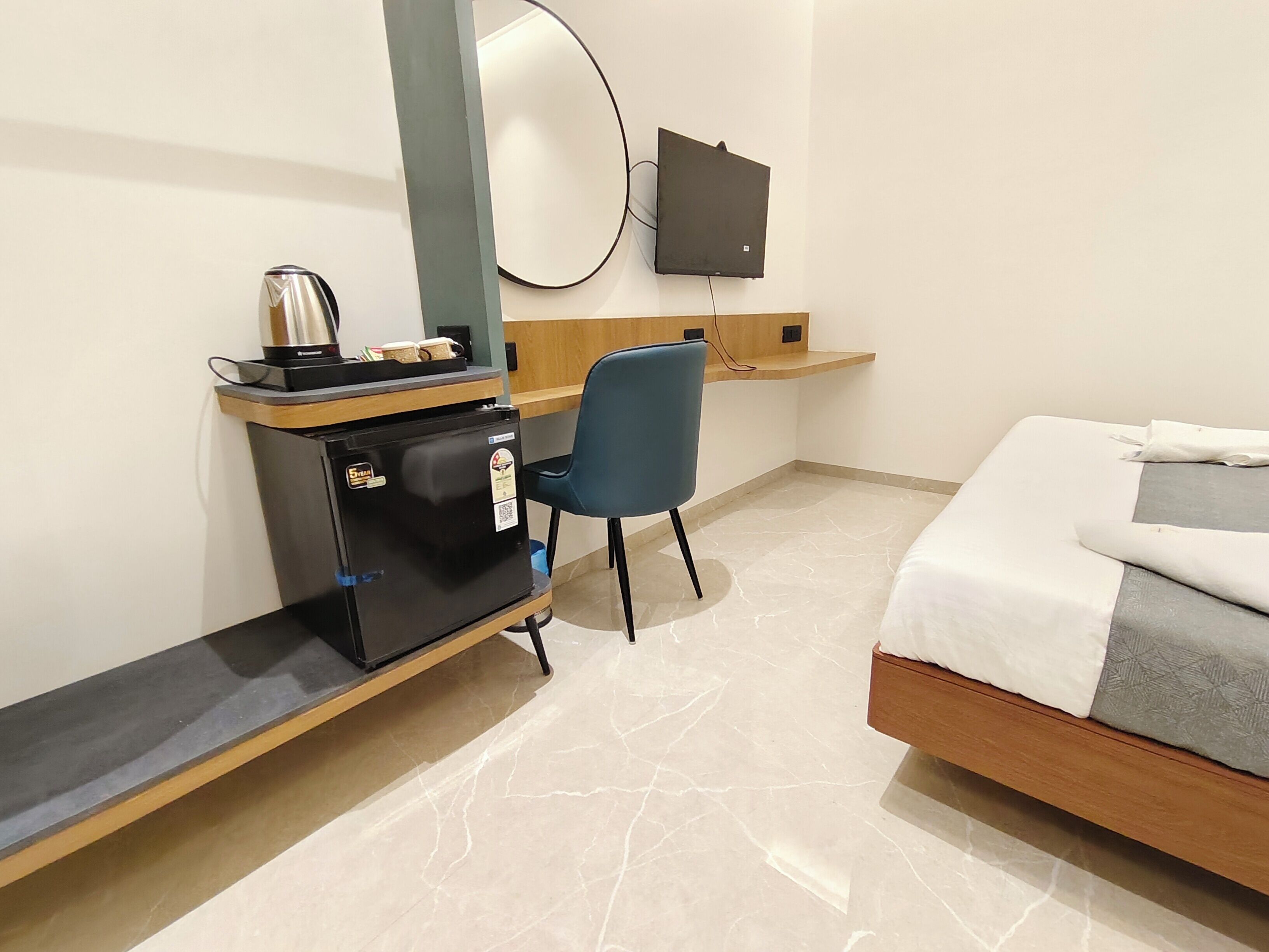 Habitación de hotel con una cama, un escritorio con computadora, una silla, un refrigerador pequeño, un espejo y un televisor de pantalla plana montado en la pared.
