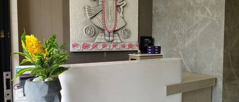 A reception desk with a statue of a deity, a potted plant, and a small table with boxes.