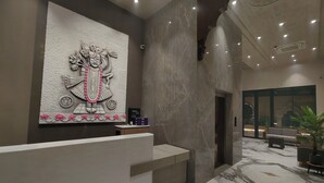 Un espace d’accueil doté d’un comptoir de réception en marbre, d’une grande sculpture murale et d’un aménagement intérieur moderne.