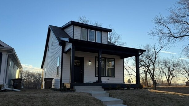 Une maison à deux étages avec un porche à l’avant, un numéro bien visible « 702 » et un escalier menant à la porte d’entrée.