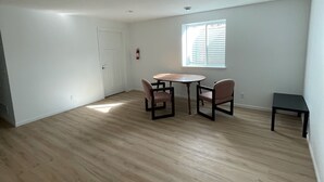 Une pièce spacieuse avec un plancher en bois, une table à manger avec des chaises, une fenêtre avec des stores et une porte.