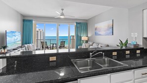 A modern kitchen with a black granite countertop, stainless steel sink, and white cabinets. - Ariel Dunes I 1306 (Miramar Beach)