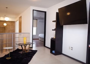 A modern hotel room with a balcony, a dining area with a table and chairs, a black rug, and a TV mounted on the wall.