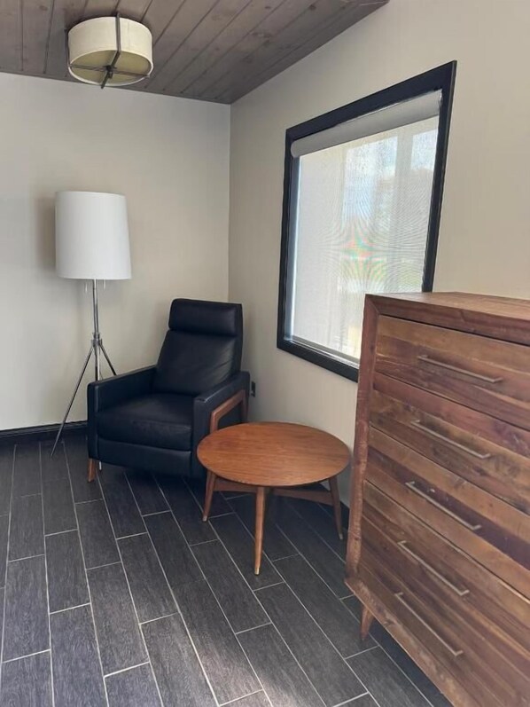 A room with a black leather chair, a small wooden table, a floor lamp, and a wooden cabinet.