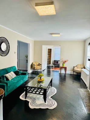 Un salon moderne avec un canapé vert, une table basse en verre ornée d’un vase de fleurs et un tapis noir et blanc.
