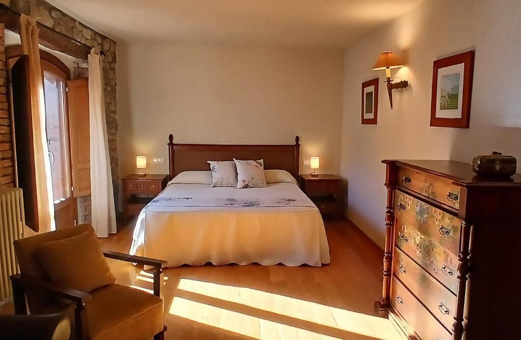 Un dormitorio con una cama grande, cabecera de madera, dos mesitas de noche con lámparas, un aparador de madera y una silla.