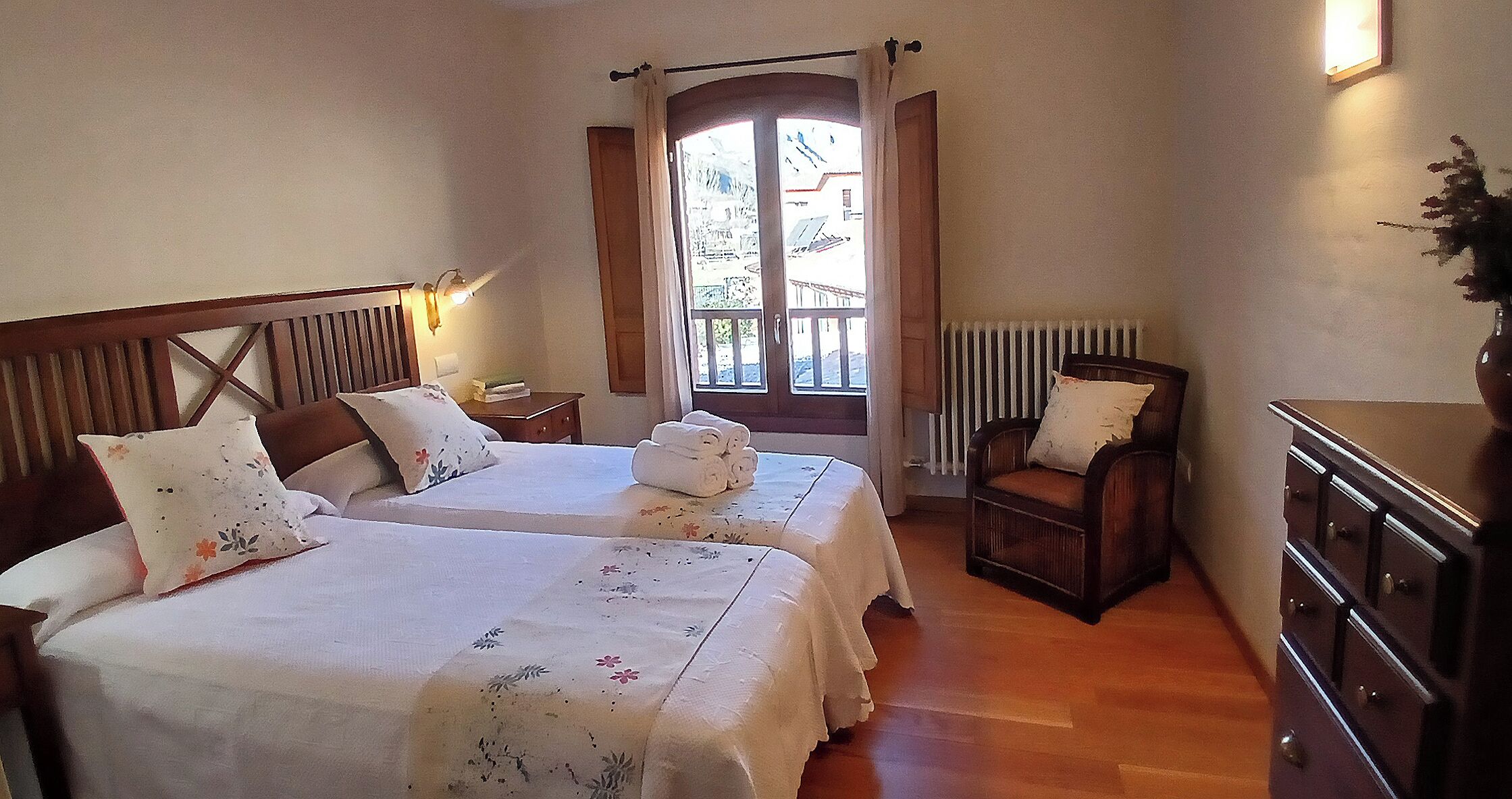 Une chambre d’hôtel avec deux lits, une chaise en bois, une commode et une fenêtre avec des rideaux.