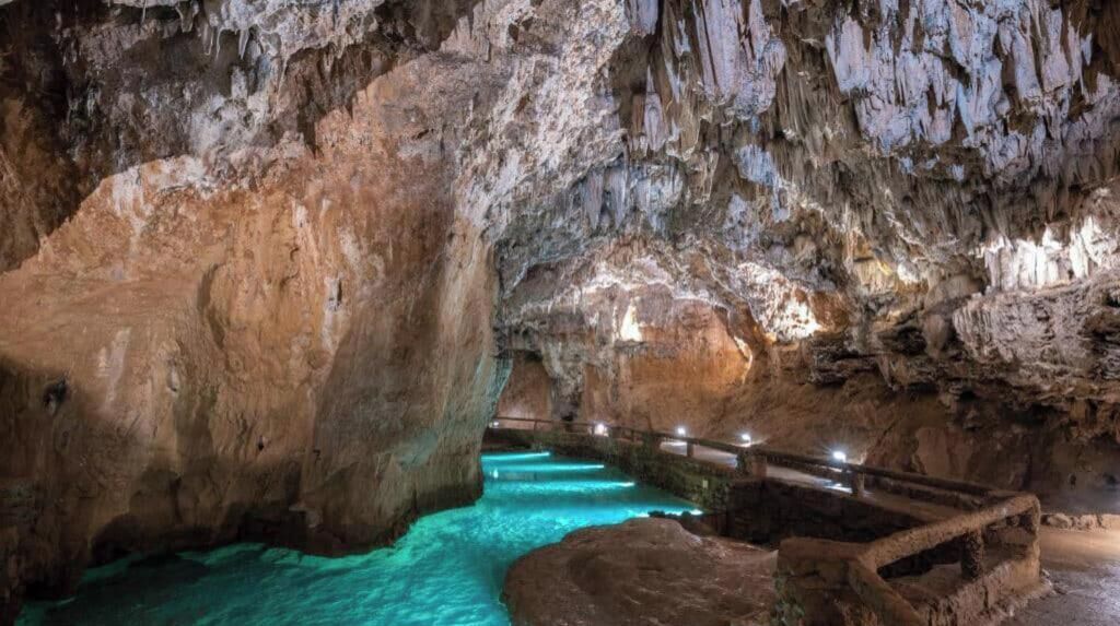 A cave interior with a turquoise pool, rocky formations, and a wooden walkway.