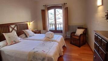Habitación de hotel con dos camas, un aparador de madera, una silla y una ventana con cortinas.