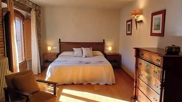 Een slaapkamer met een groot bed, twee nachtkastjes met lampen, een houten dressoir en een stoel.
