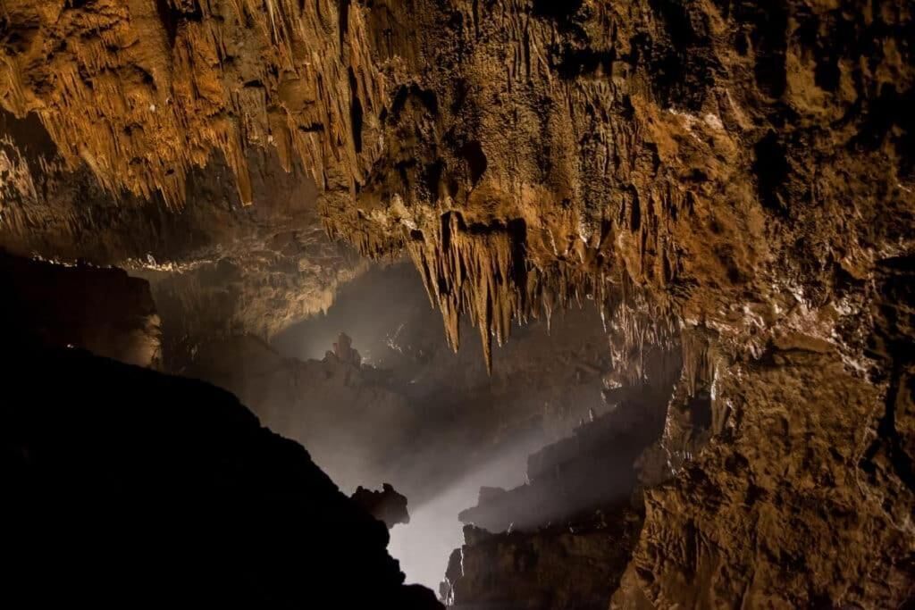 A cave interior with stalactites and stalagmites, dim lighting, and a misty atmosphere.