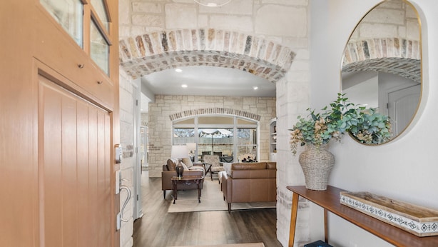 A spacious living area with a stone archway, a wooden door, a console table with a vase, and a mirror.