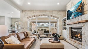 A cozy living room with a stone fireplace, leather sofas, and a large window overlooking a scenic view.